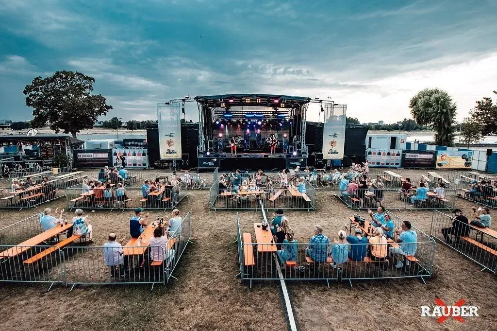 Bei einem Konzert sitzt eine Gruppe von Menschen an Tischen vor einer Bühne.
