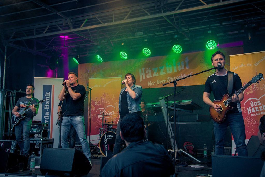 Eine Gruppe Männer steht auf einer Bühne, spielt Gitarre und singt in Mikrofone.