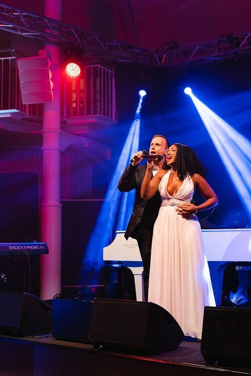 Ein Mann und eine Frau singen auf einer Bühne vor einem Klavier.