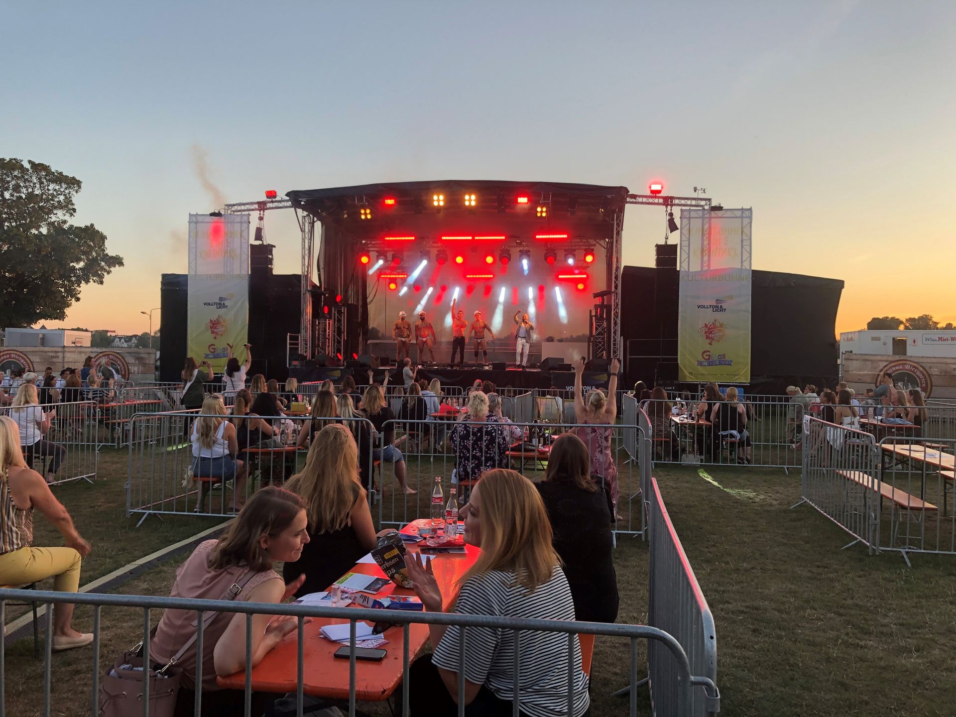 Bei einem Konzert sitzt eine Gruppe von Menschen an Tischen vor einer Bühne.