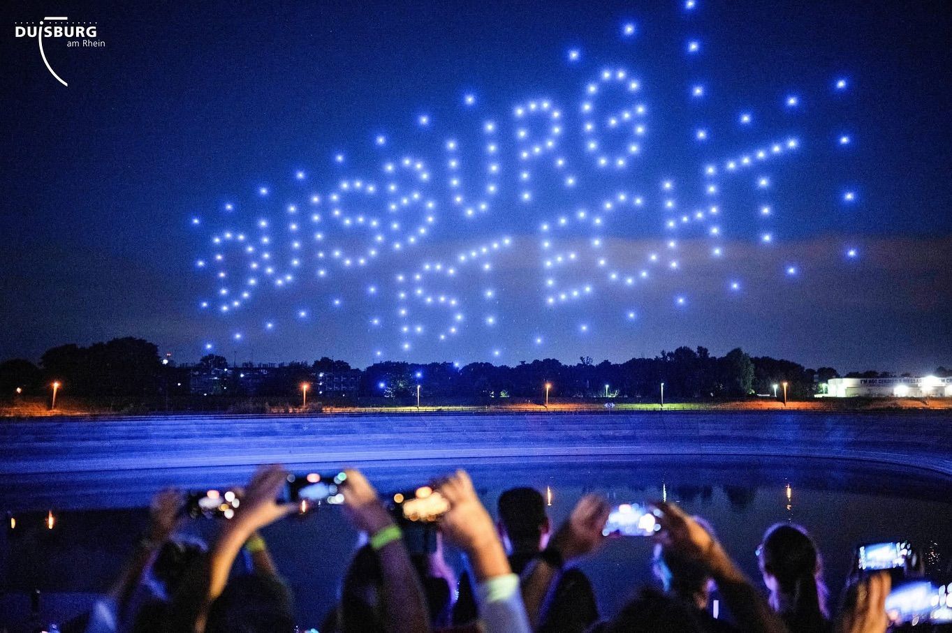 See mit Dronenschow darüber und Menschen die Filmen