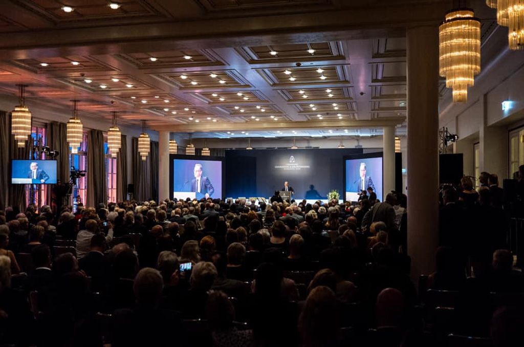 Eine große Gruppe von Menschen sitzt in einem großen Raum und sieht sich eine Präsentation an.