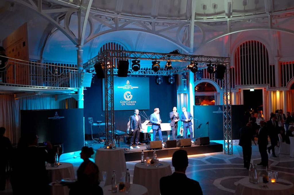 Eine Gruppe von Menschen sitzt an Tischen vor einer Bühne.