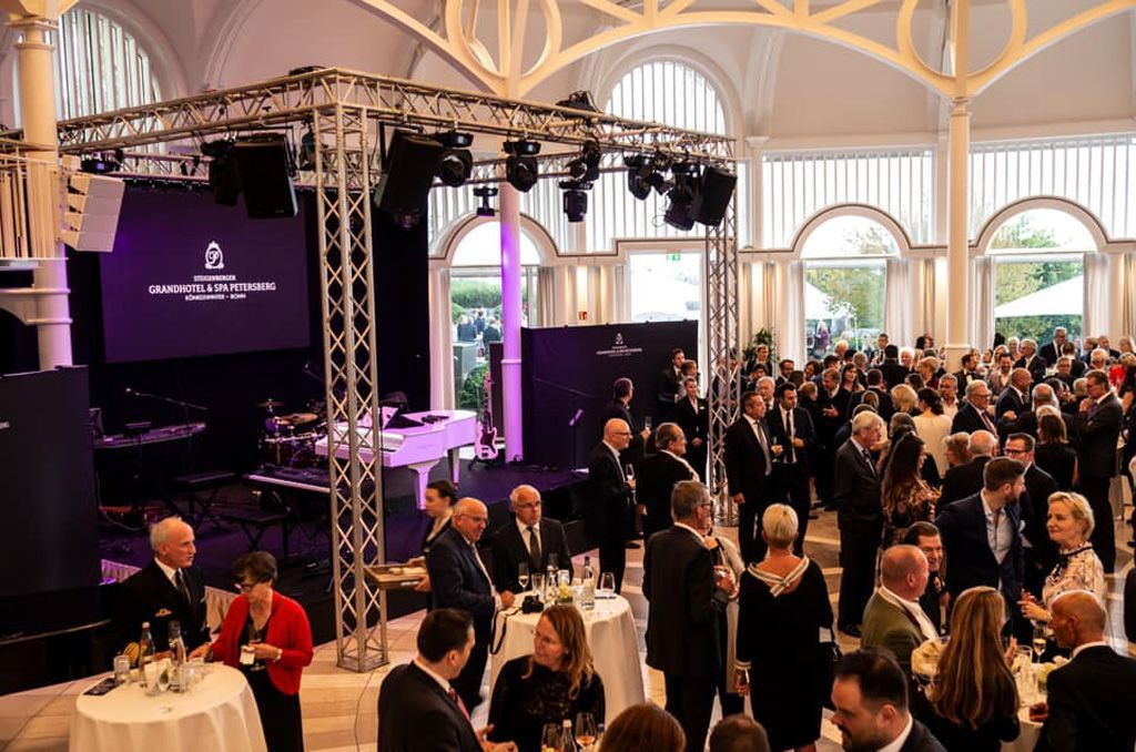 Eine große Gruppe von Menschen steht in einem großen Raum um Tische herum.