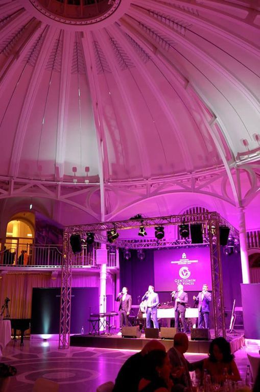 Eine Gruppe von Menschen sitzt an Tischen vor einer Bühne mit violetten Lichtern