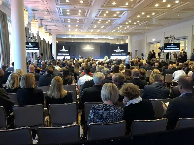Eine große Gruppe von Menschen sitzt in einem großen Raum und sieht sich eine Präsentation an.