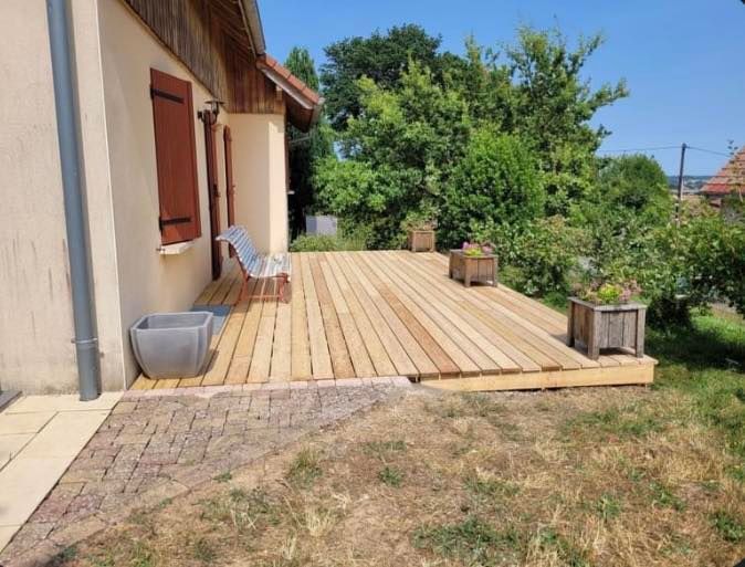 Une terrasse en bois d'une maison aux volets de couleurs ocre.