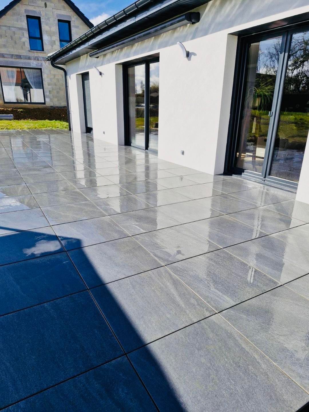 Terrasse brillante au pied d'une habitation avec des grandes baies vitrées.