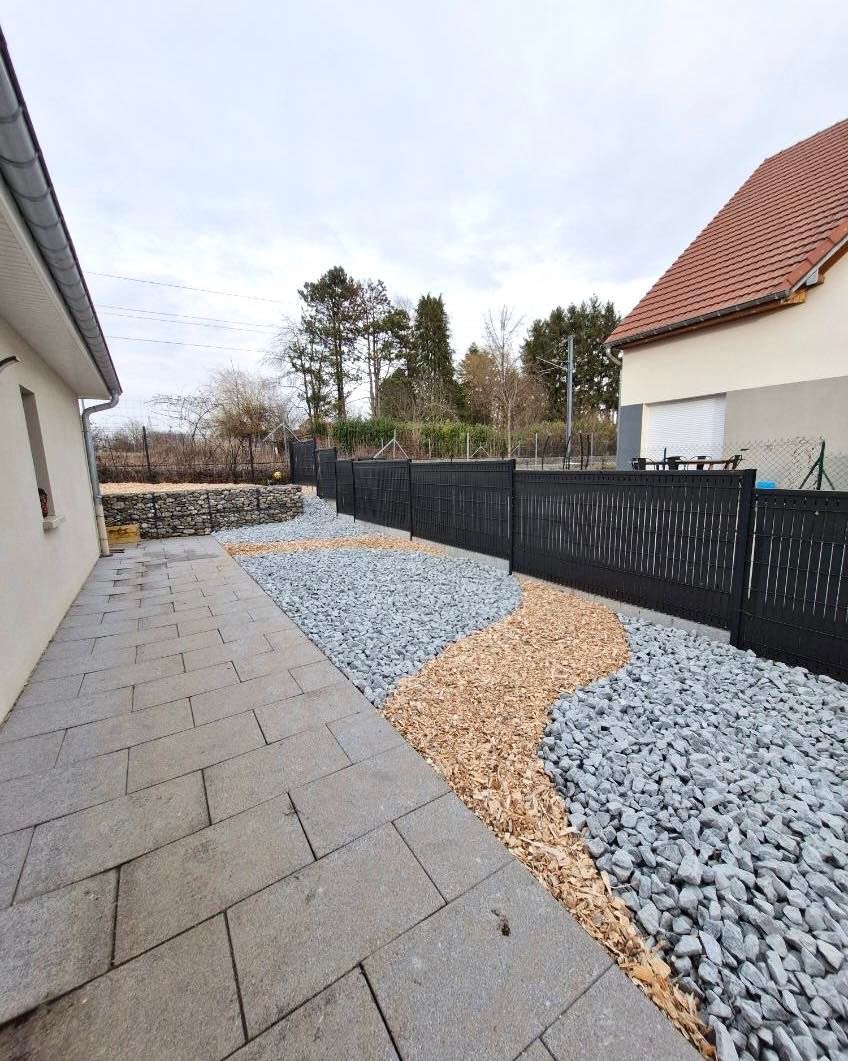 Allée contournant la maison avec vue sur une clôture noir anthracite.