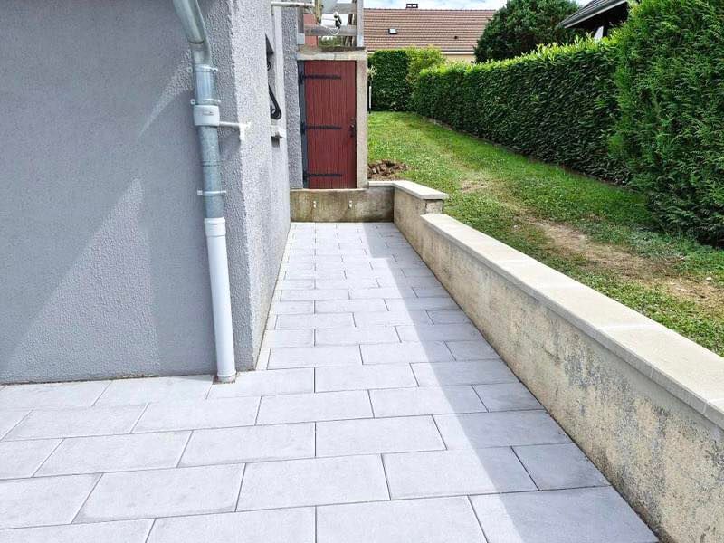 Allée faisant le contour de la maison et menant vers une porte de couleur bordeaux.