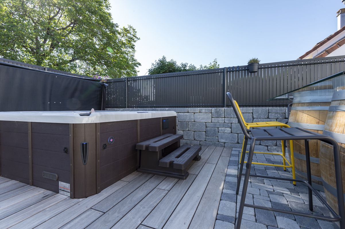 Spa ouvert dans l'angle d'une terrasse en bois au pied de la clôture.