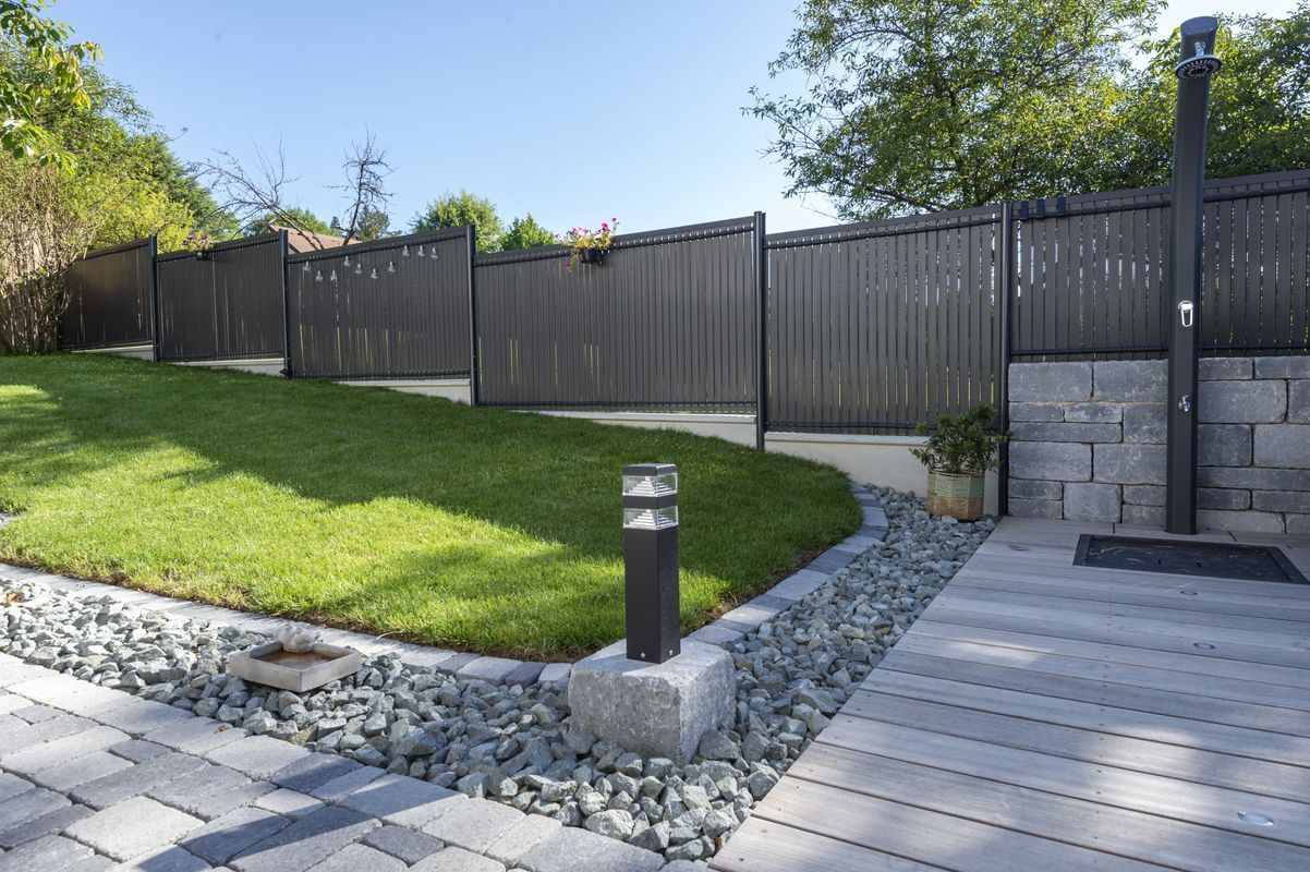 Lumière extérieure posée dans l'angle d'un passage devant une clôture en aluminium.