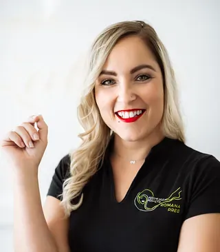 Frau mit blonden Haaren und rotem Lippenstift lächelt, trägt ein schwarzes T-Shirt mit Logo, in einem weißen Raum.