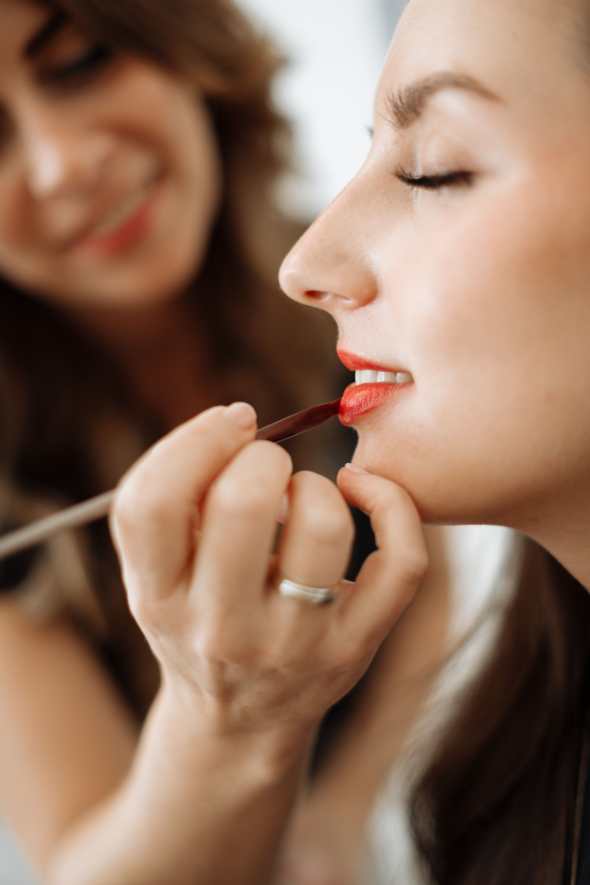 Eine Visagistin trägt Lippenstift auf die Lippen einer Frau auf.