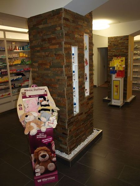 Apothekeninterieur mit einer Steinsäule, Regalen mit Produkten und einem Ausstellungsständer mit Plüschtieren.