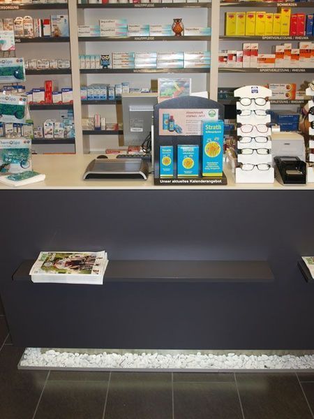 Apothekentheke mit Medikamentenauslagen und Regalen voller Produkte.