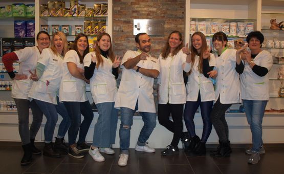 Eine Gruppe von neun Personen in weissen Kitteln lächelt und posiert in einer Apotheke.