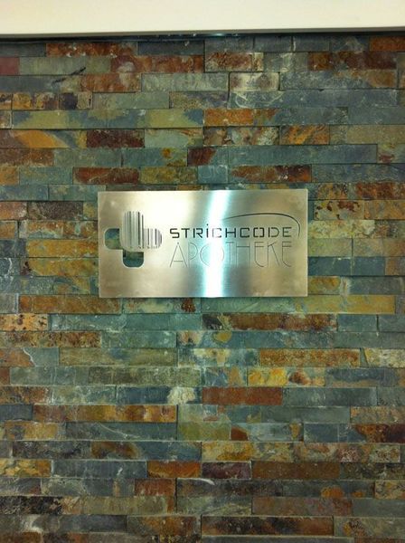Silbernes Schild mit der Aufschrift „STRICHCODE“ und einem Symbol, angebracht an einer Backsteinmauer.