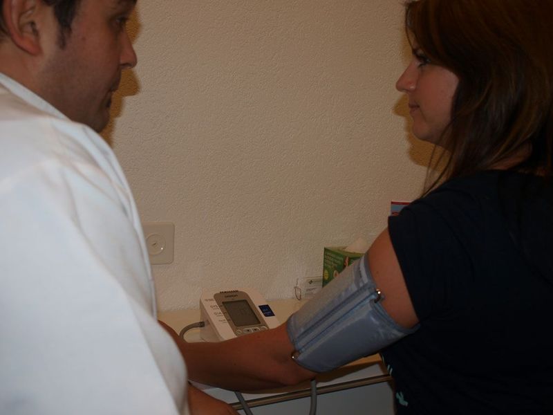 Ein Arzt misst den Blutdruck eines Patienten mit einer Oberarmmanschette und einem digitalen Blutdruckmessgerät.