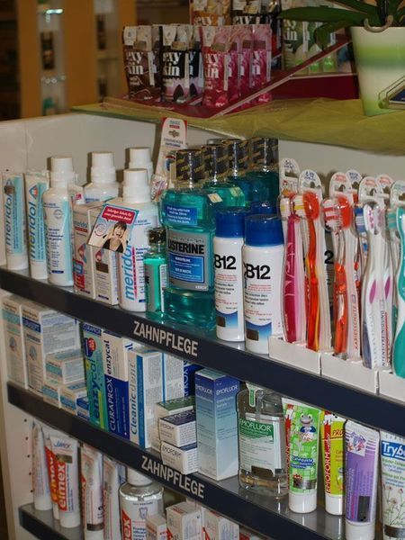Regalauslage in einer Apotheke: verschiedene Zahnhygieneprodukte, darunter Mundwasser, Zahnbürsten und Zahnpasta.