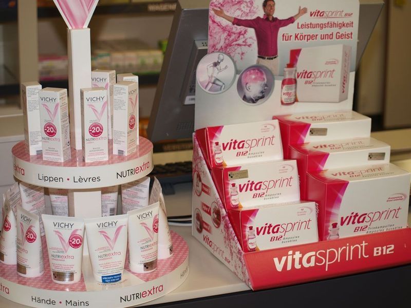 Verkaufsständer mit Hautpflegeprodukten und Vitaminen in einem Geschäft. Überwiegend rosa und weisse Verpackung.