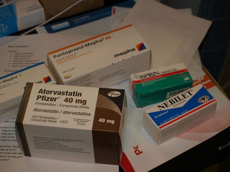 Auf einem Tisch stehen mehrere Schachteln mit verschreibungspflichtigen Medikamenten, darunter Atorvastatin, Pantoprazol, Aspirin und Nebilet.
