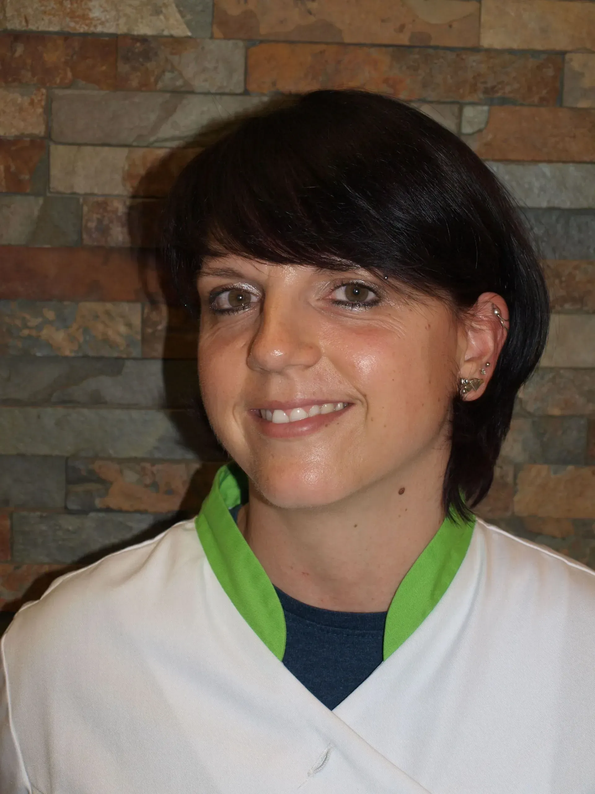 Frau in einem weissen Kittel lächelt vor einer Steinmauer.