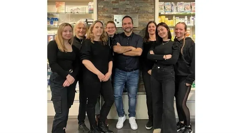 Eine Gruppe von neun Personen posiert in einem Geschäft, alle lächeln, einige haben die Arme verschränkt.