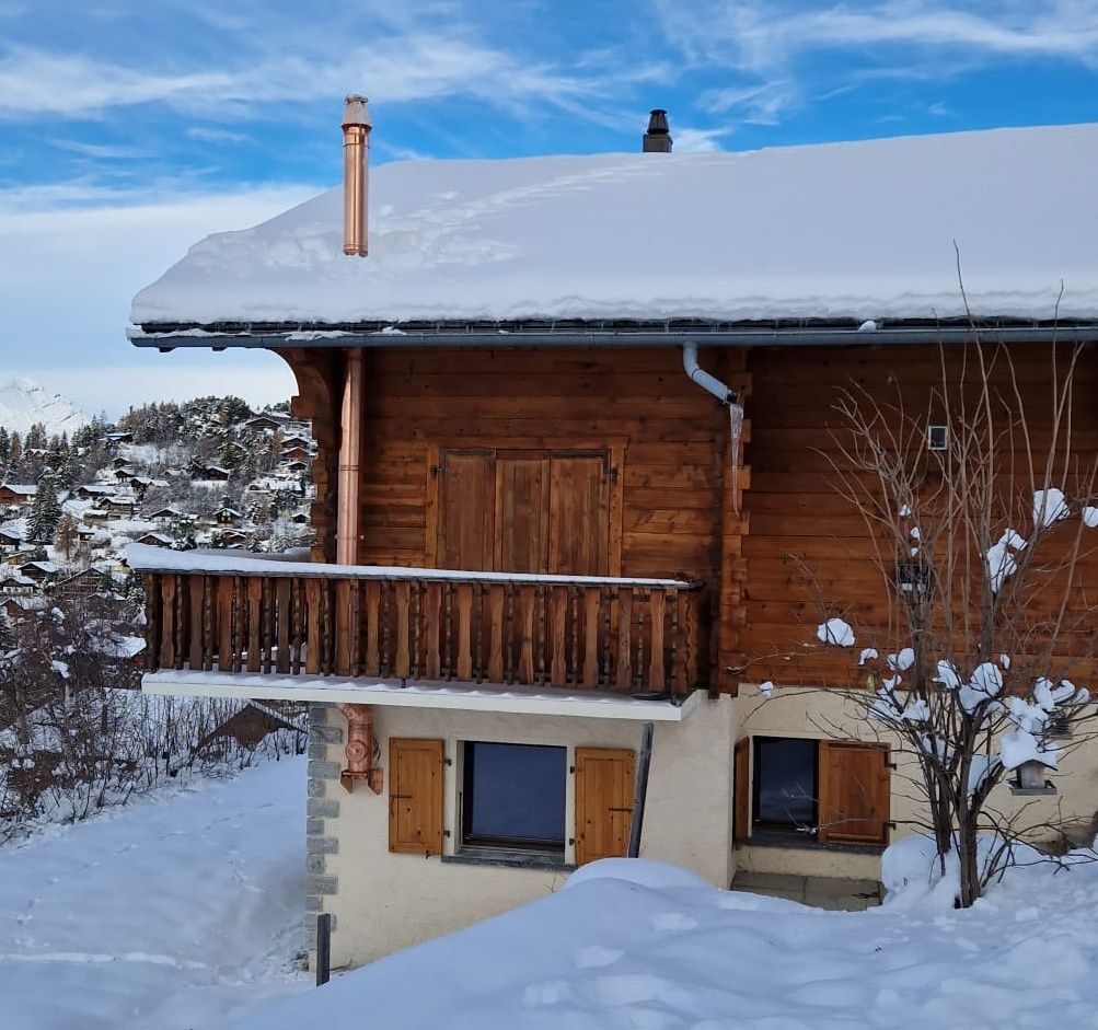 Chalet en bois recouvert de neige, avec balcon et cheminée en cuivre