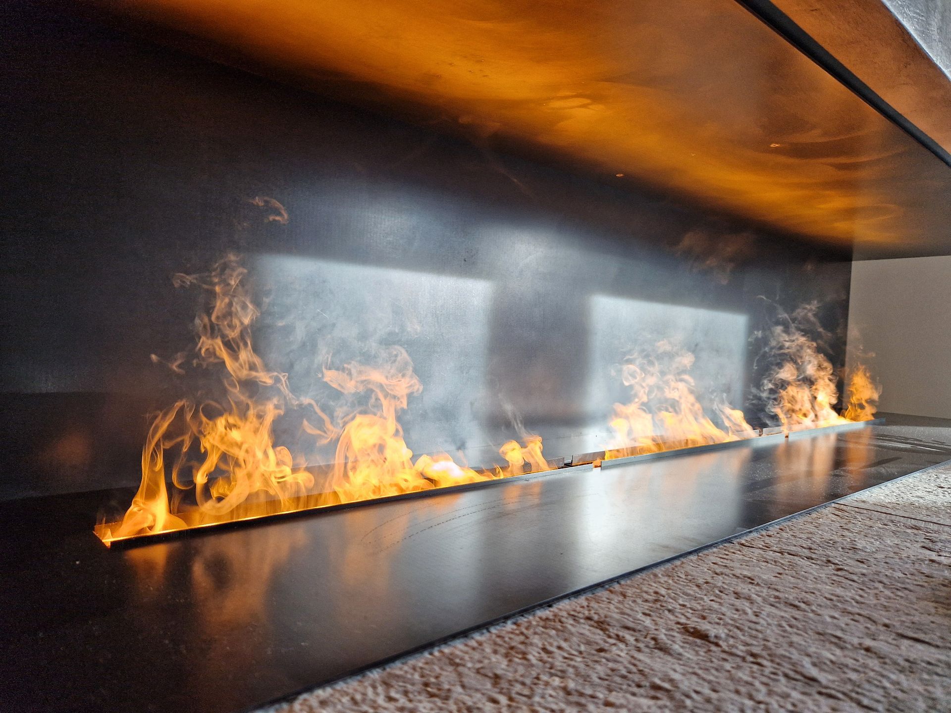 Des flammes jaillissent d'une fente horizontale dans une surface sombre et noire ; fumée et brume de chaleur visibles.