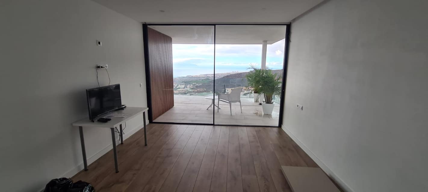 Una habitación con una mesa, televisión y puertas corredizas de vidrio que conducen a un balcón.