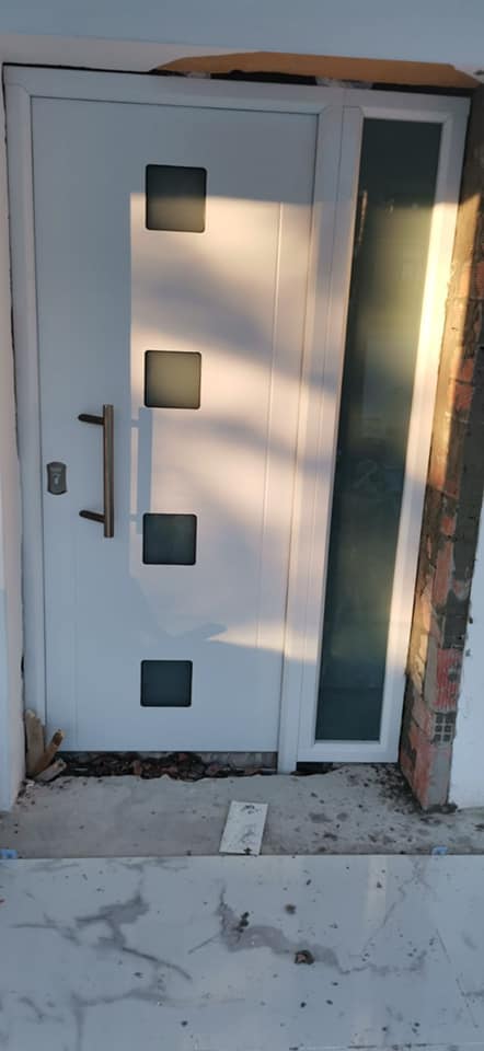 Una puerta blanca con cuadrados está al lado de una pared de ladrillos.