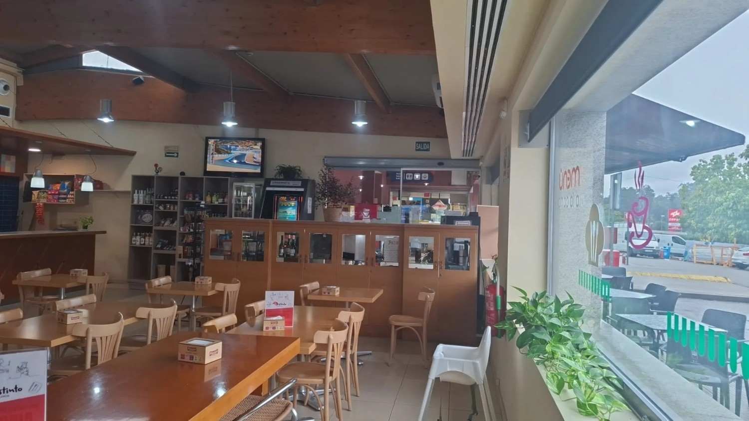 Acogedor interior de cafetería con mesas de madera, estanterías y un gran ventanal con vistas a la calle