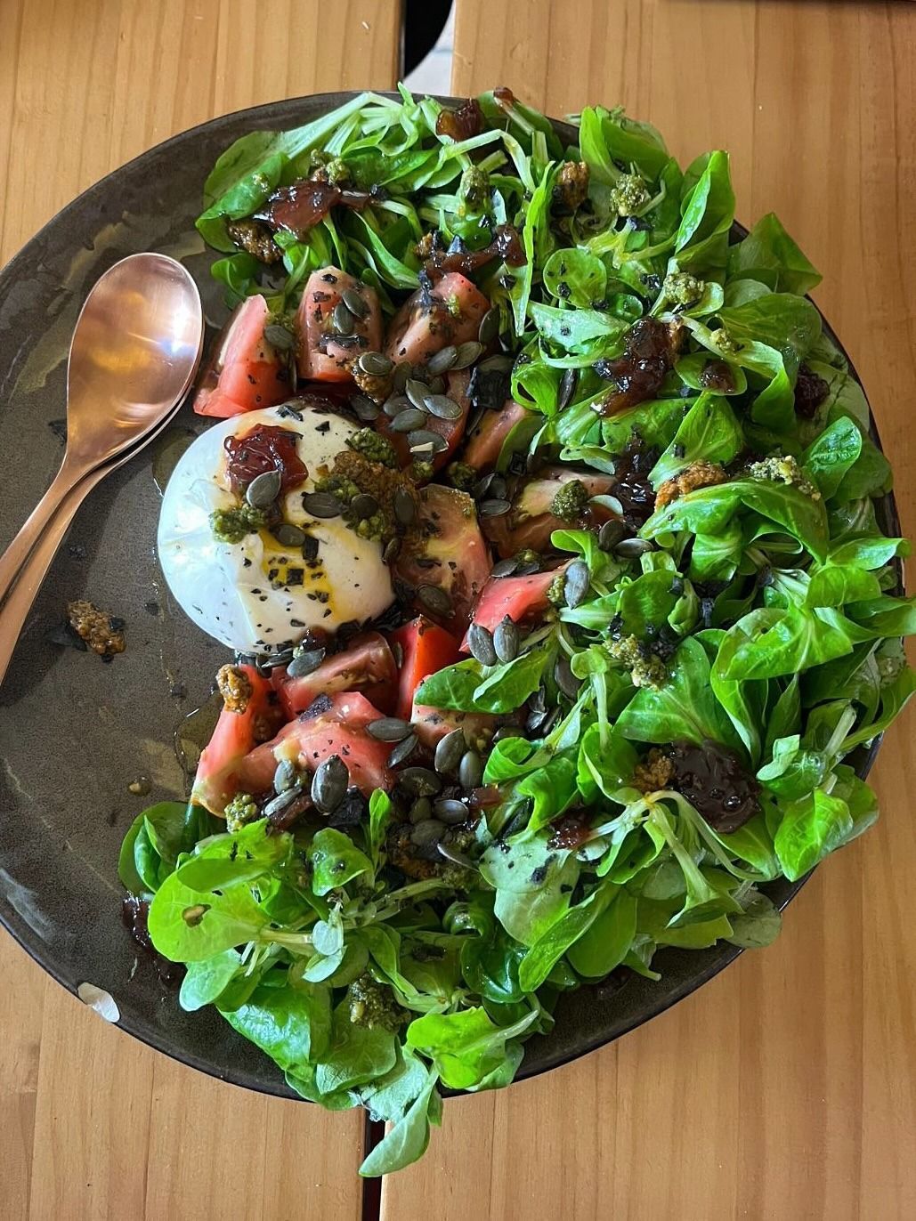 Bol de ensalada con verduras, fresas, huevo escalfado y aderezo sobre una mesa de madera.