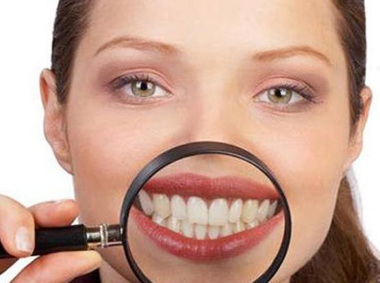 Mujer sonriendo con dientes magnificados por una mano que sostiene una lupa.