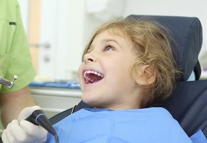 Niño en la silla del dentista, riendo con la boca abierta, mirando hacia arriba; herramientas dentales visibles.