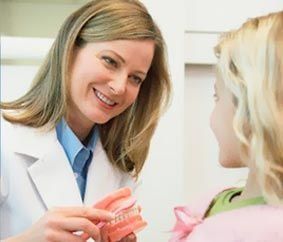 Dentista mostrando un modelo dental a un paciente joven. Sonríe. Entorno clínico.
