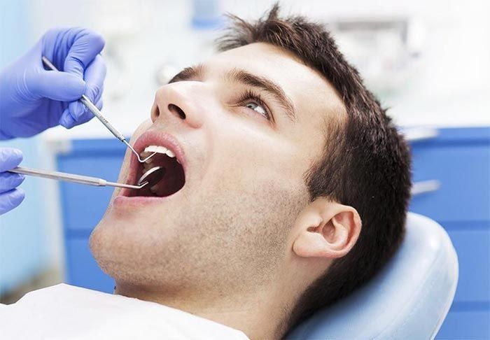 Hombre en silla dental con la boca abierta, herramientas dentales en uso.
