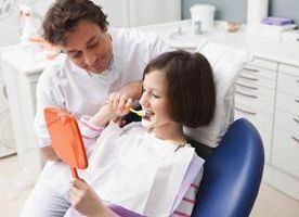 Dentista enseñando a un paciente a cepillarse los dientes en una consulta. El paciente sostiene un espejo.