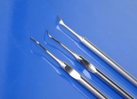 Tres bisturíes quirúrgicos de acero inoxidable sobre una superficie azul.