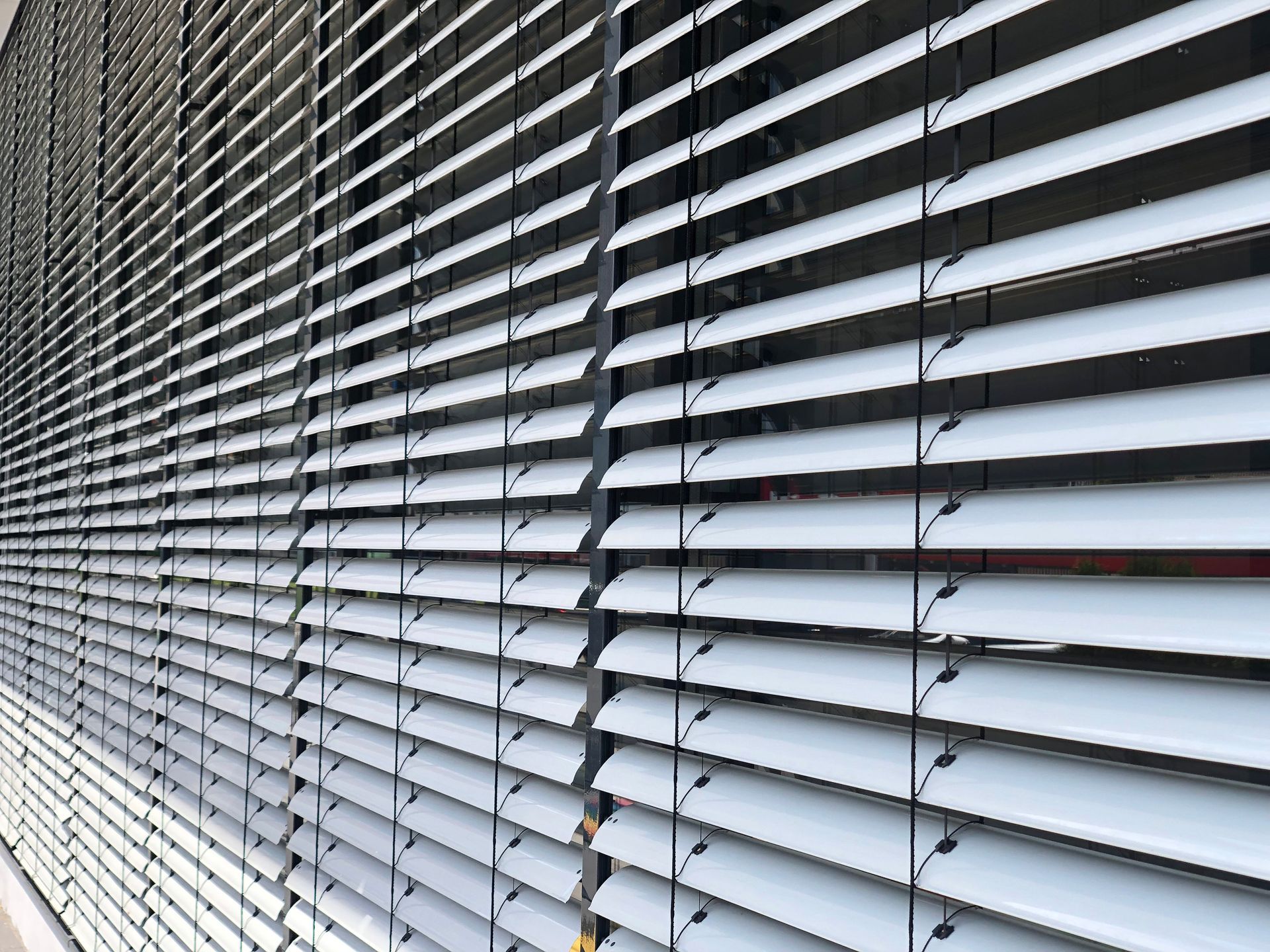 Metallene Jalousien mit teilweise geöffneten Lamellen, durch die Licht durch das Fenster fällt.