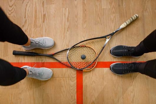 Zwei Squash-Schläger auf dem Boden, zwischen Spielerinnen