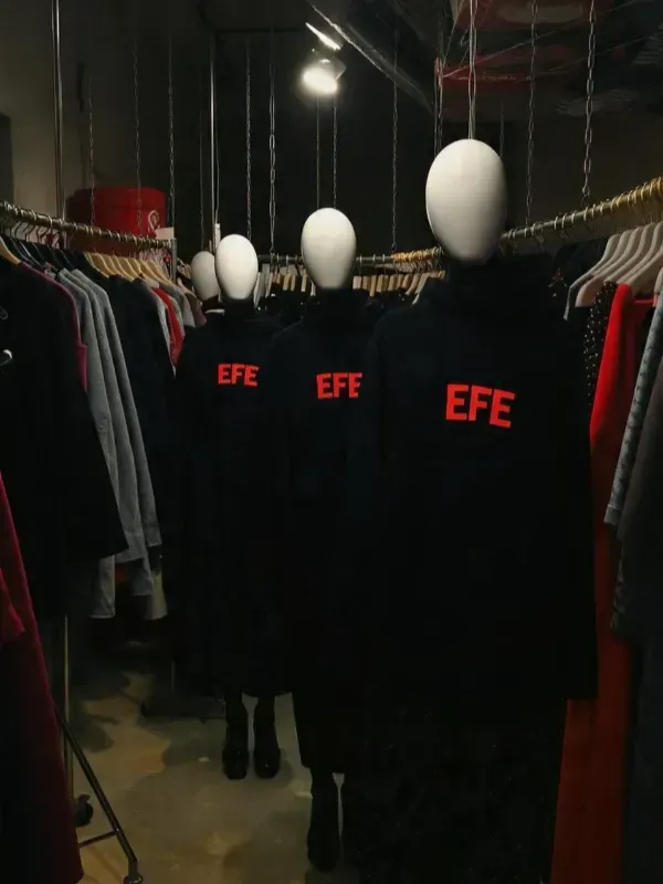 Un perchero con camisetas negras de EFE y cabezas de maniquí blancas en una tienda con poca luz.