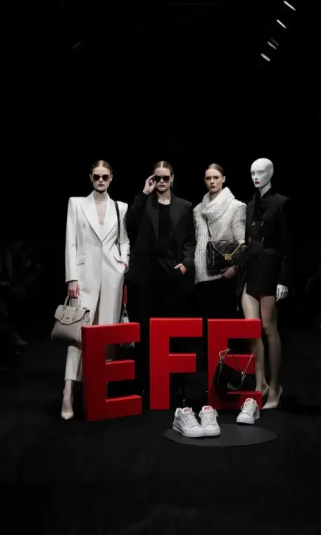 Cuatro personas con elegantes atuendos en blanco y negro posando detrás de grandes letras rojas 