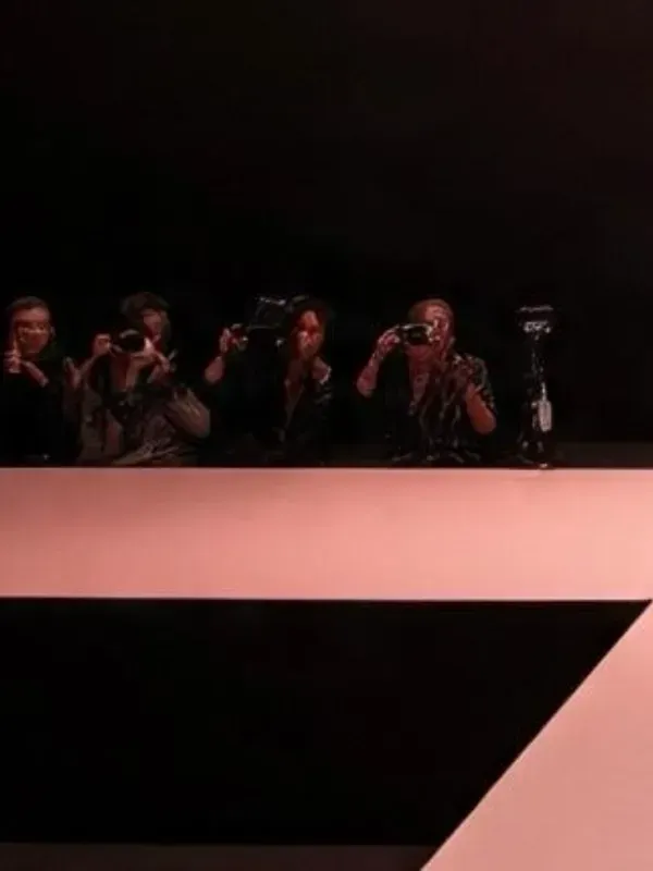 Fotógrafos tomando fotos desde un balcón oscuro detrás de una barrera rosa.