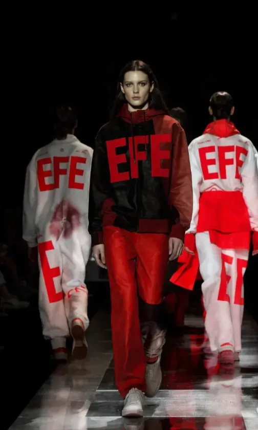 Tres modelos sin rostro, vestidas con atuendos negros y logotipos rojos de EFE, caminan hacia la cámara.