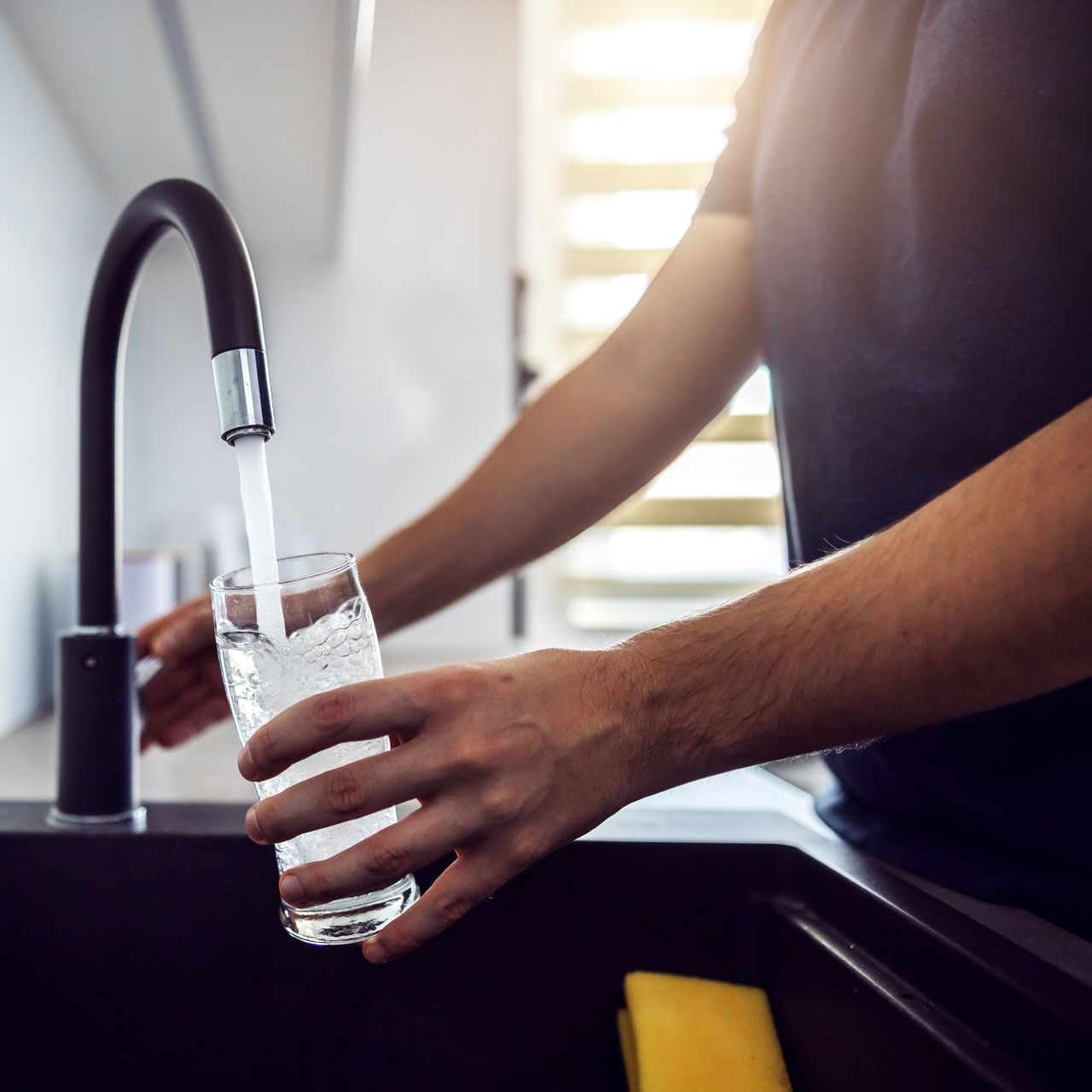 Une personne remplit un verre transparent d'eau provenant d'un robinet de cuisine.
