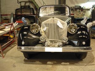 Coche negro clásico en un taller, con la parte delantera cubierta con tela protectora y los faros envueltos.