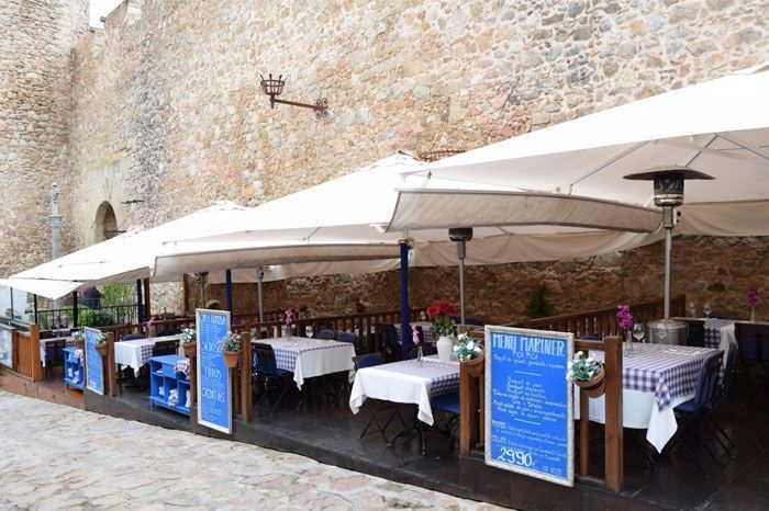 Un restaurante con mesas y sombrillas frente a un muro de piedra.