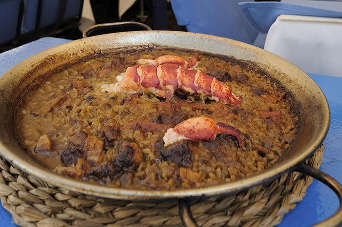 Una sartén con comida y una langosta encima, sobre una mesa.